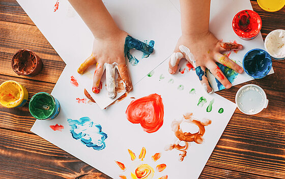 Nahaufnahme eines Kindes, das mit der Hand ein buntes Mosaik malt.